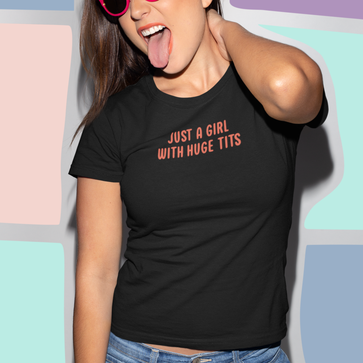 A woman wearing a black t-shirt with the text "Just a girl with huge tits" is shown making a playful and tongue-in-cheek gesture, with her tongue sticking out.